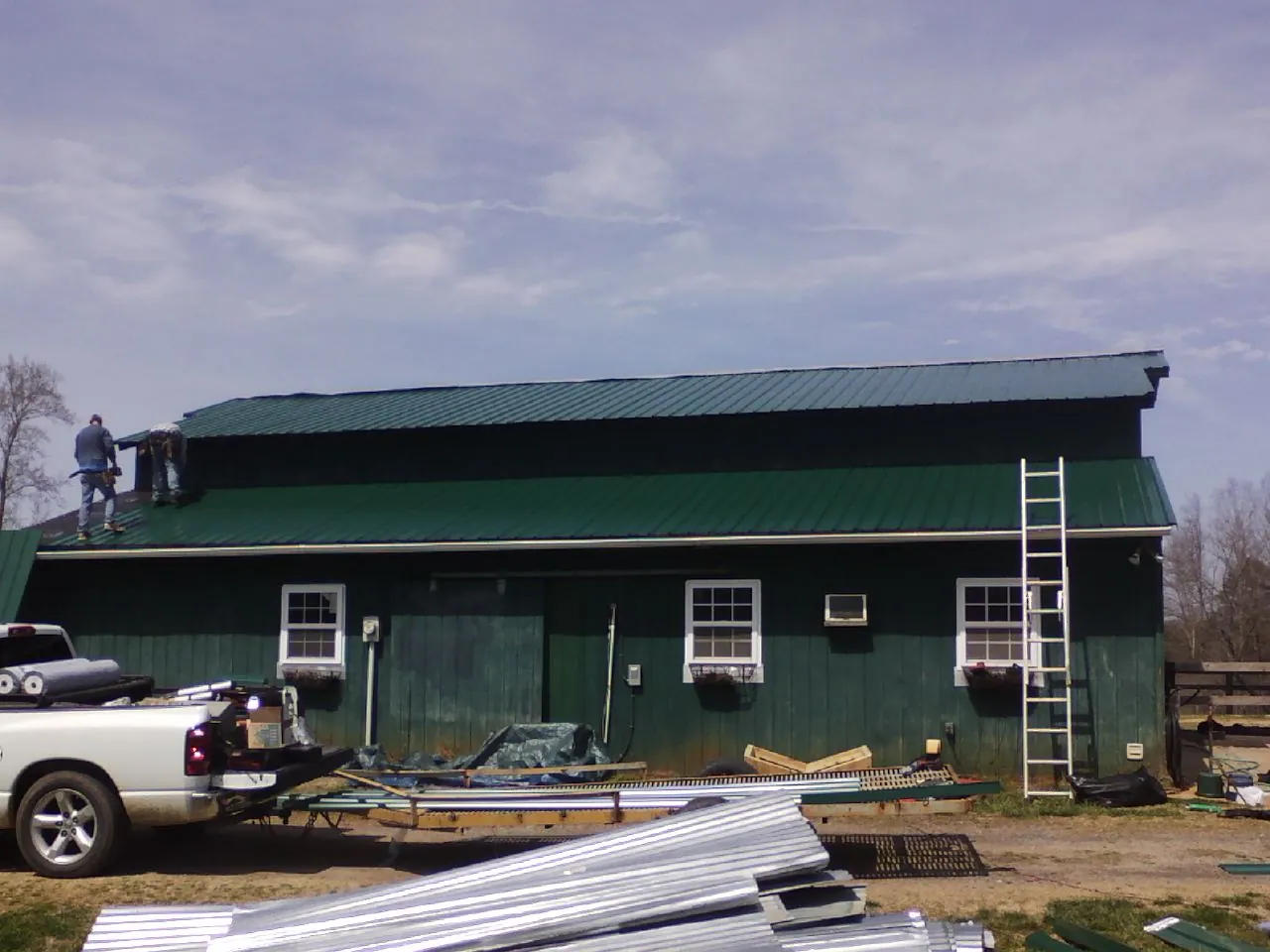 Crew installing green metal roofing on a large green barn in Jacksonville