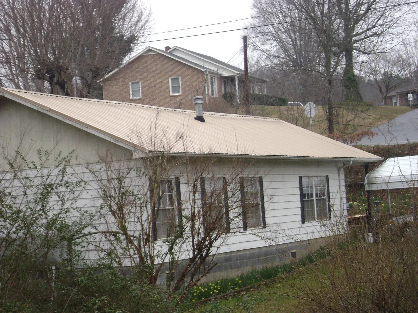 Tan metal roof on a white sided house set into a hillside — Commercial Roofing by Roofing Brothers in Jacksonville